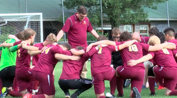 Coach praying with highschool soccer players