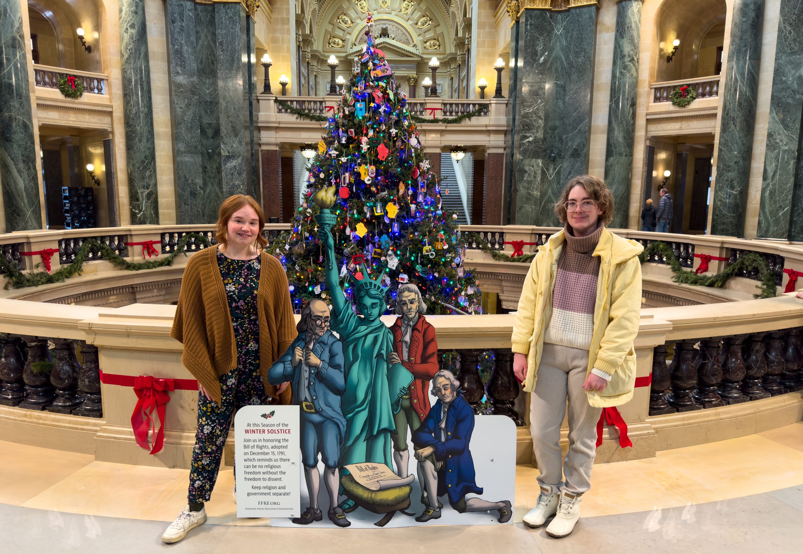 Two FFRF staff members standing with the FFRF holiday display at the Madison state capitol