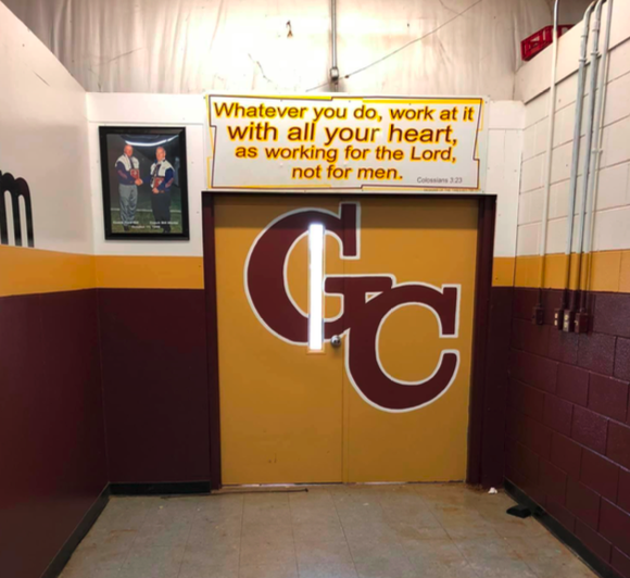 Doors in a high school hallway with a bible quote above them