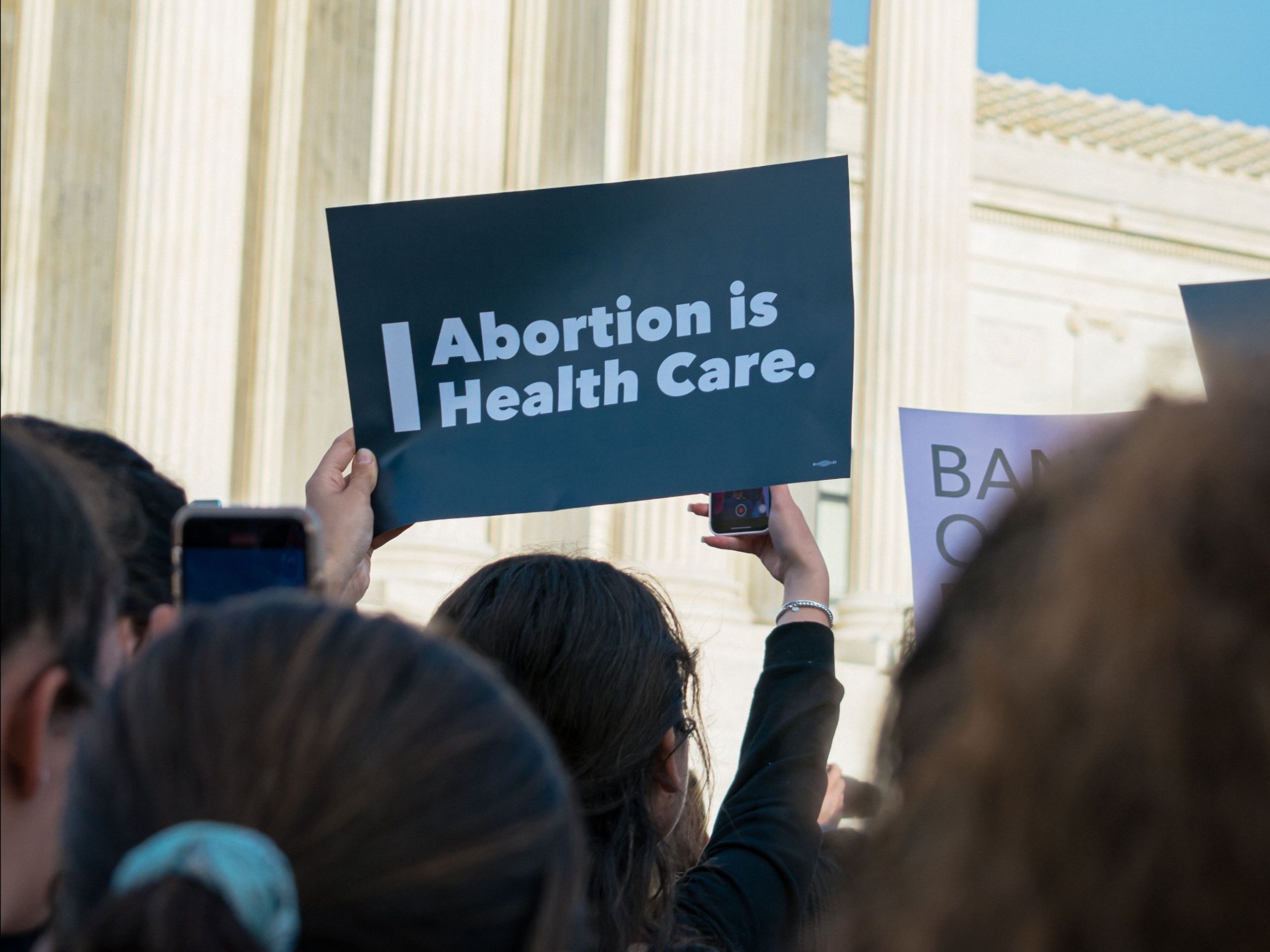 A person holding up a sign that says "Abortion is health care" in a group of people at an outdoor protest