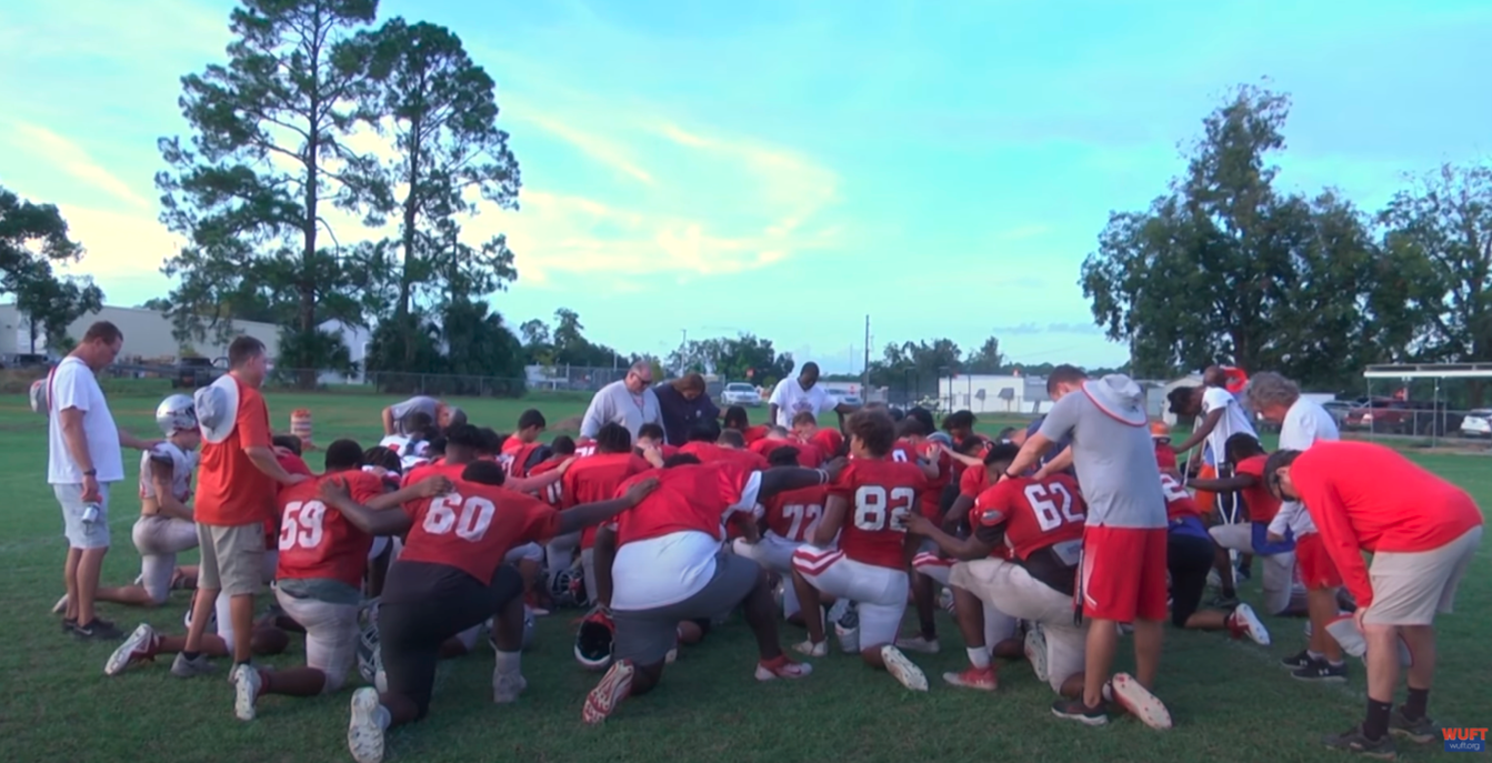 A high school football team on the field praying in a circle