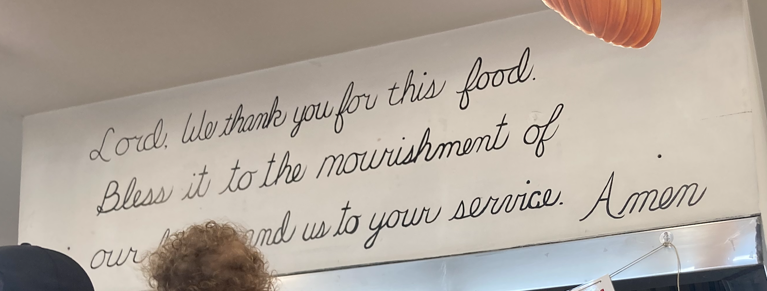 A display in a cafeteria that reads "Lord, we thank you for this food Bless it to the nourishment of our (blocked by head) us to your service. Amen."