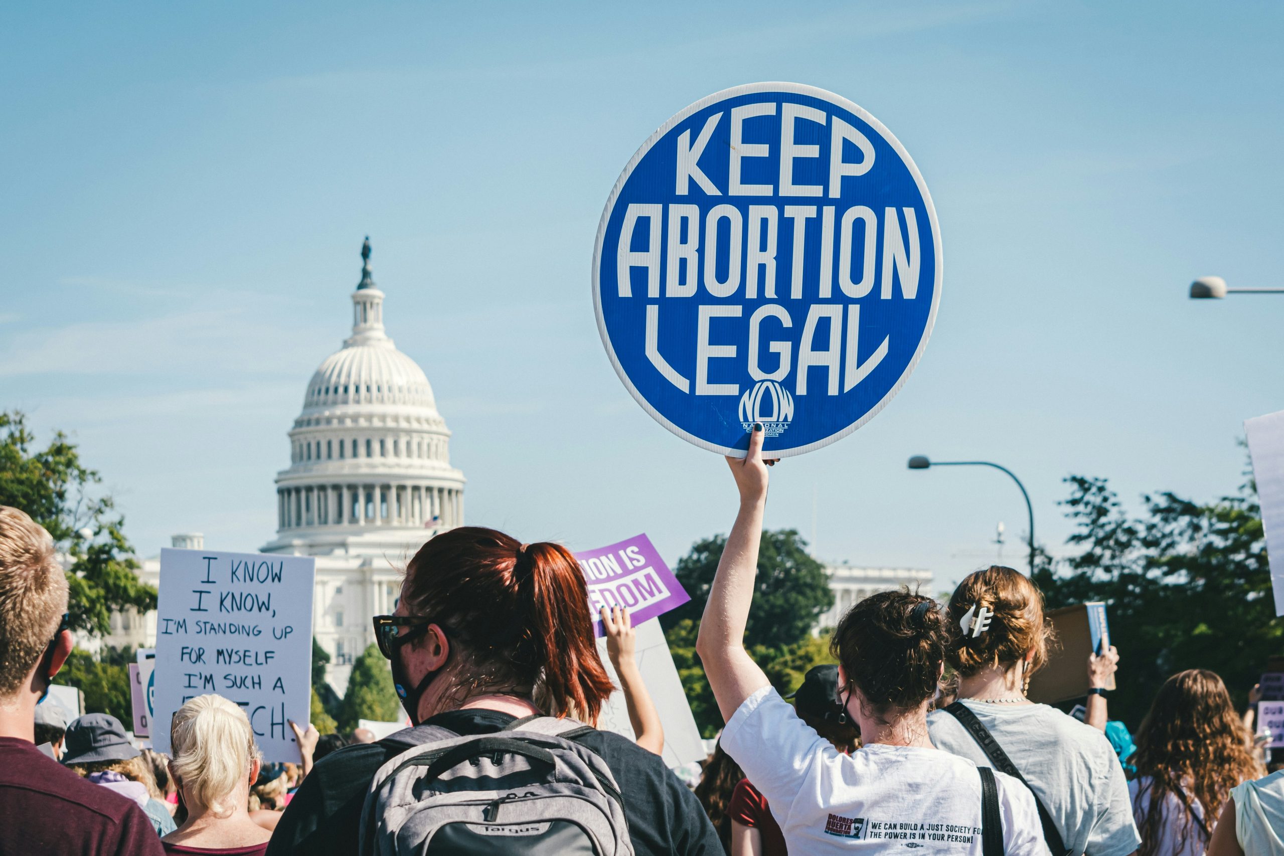 stock photograph of a protest at the US capitol building. A woman holds a blue, round sign that says "Keep Abortion Legal"