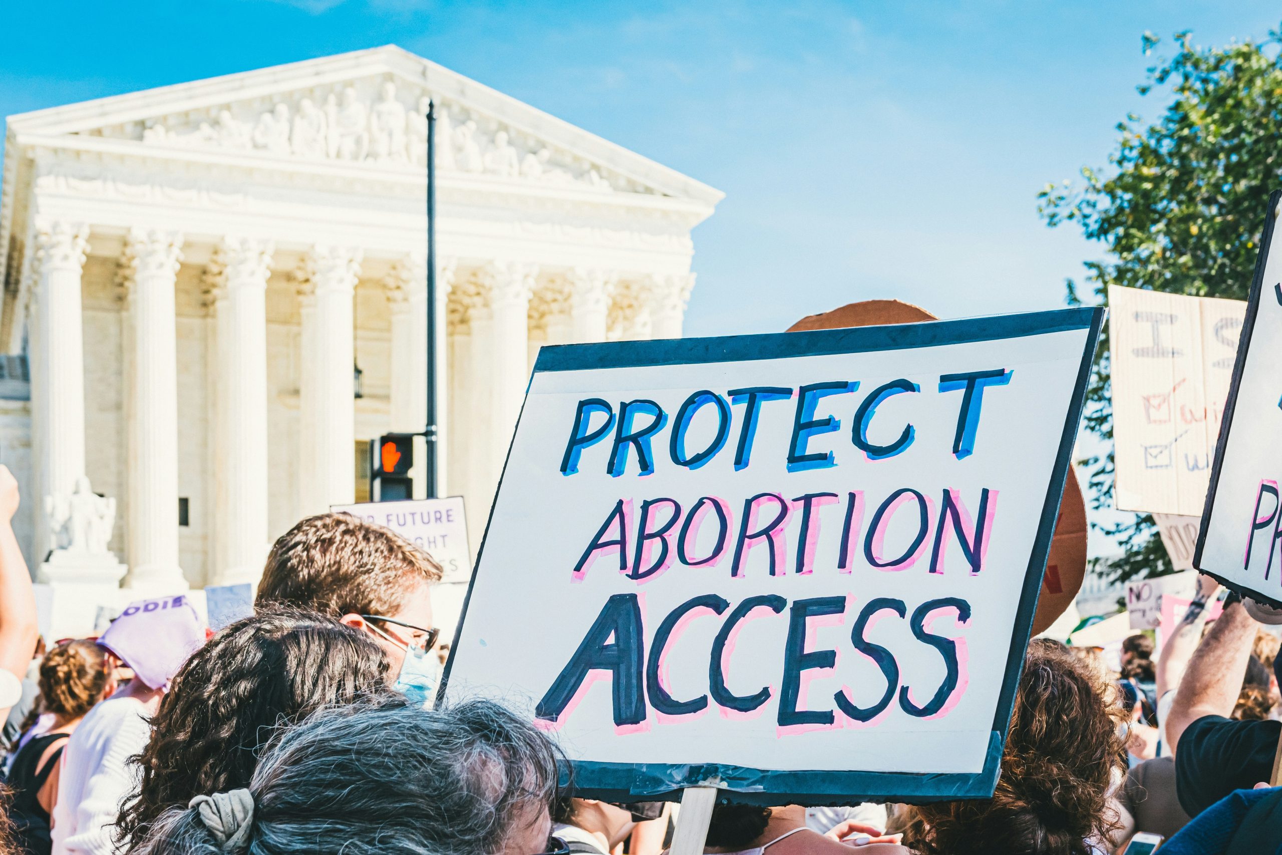 A crowd at a protest with someone holding a sign that says "Protect Abortion Access"
